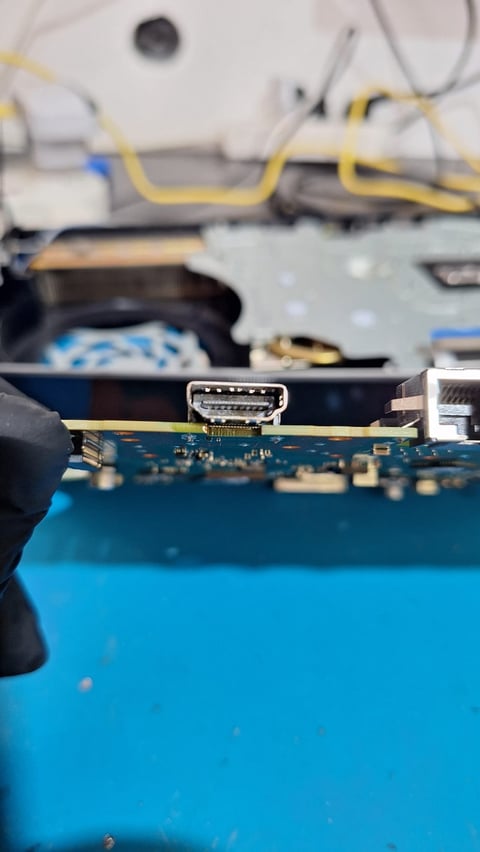 Close-up of HDMI port on blue circuit board with yellow cables and electronics visible in blurred background