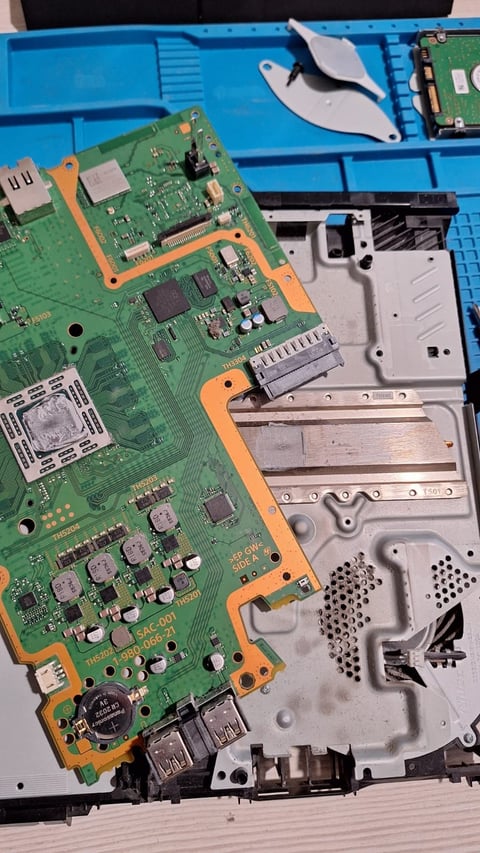 Disassembled gaming console showing green circuit board and plastic housing components on blue organizer tray